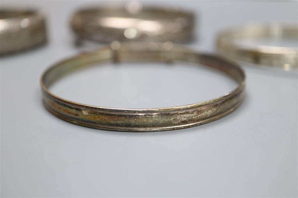 Four assorted silver bangles and a gold plated bangle.